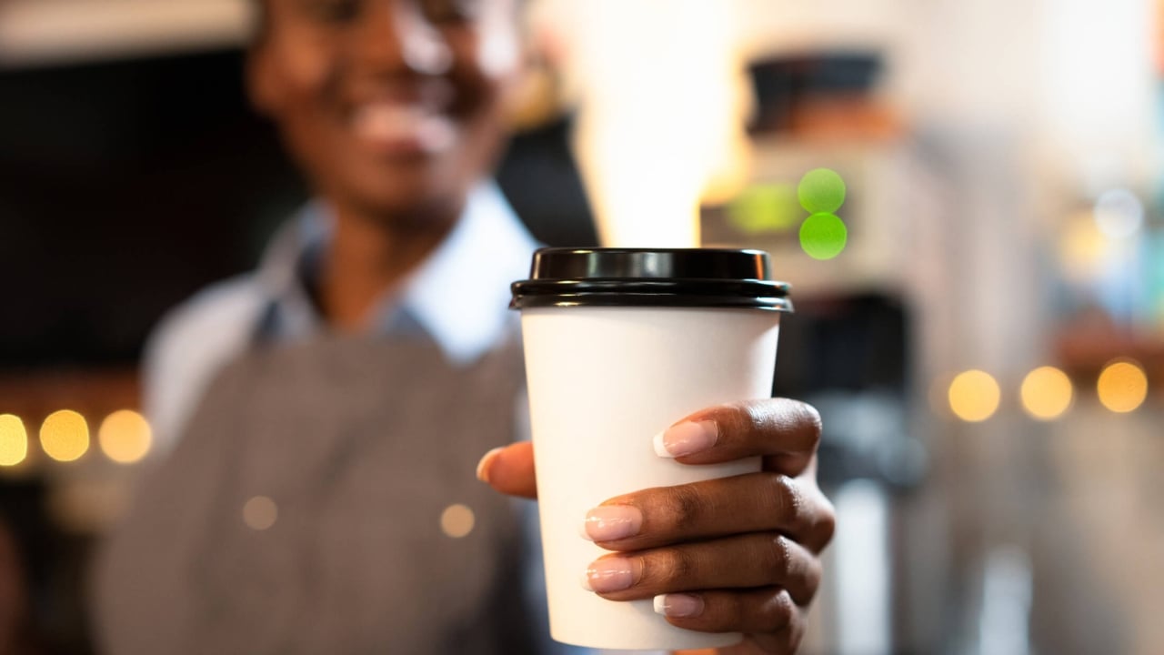 a woman holding a cup of coffee in a paper cup