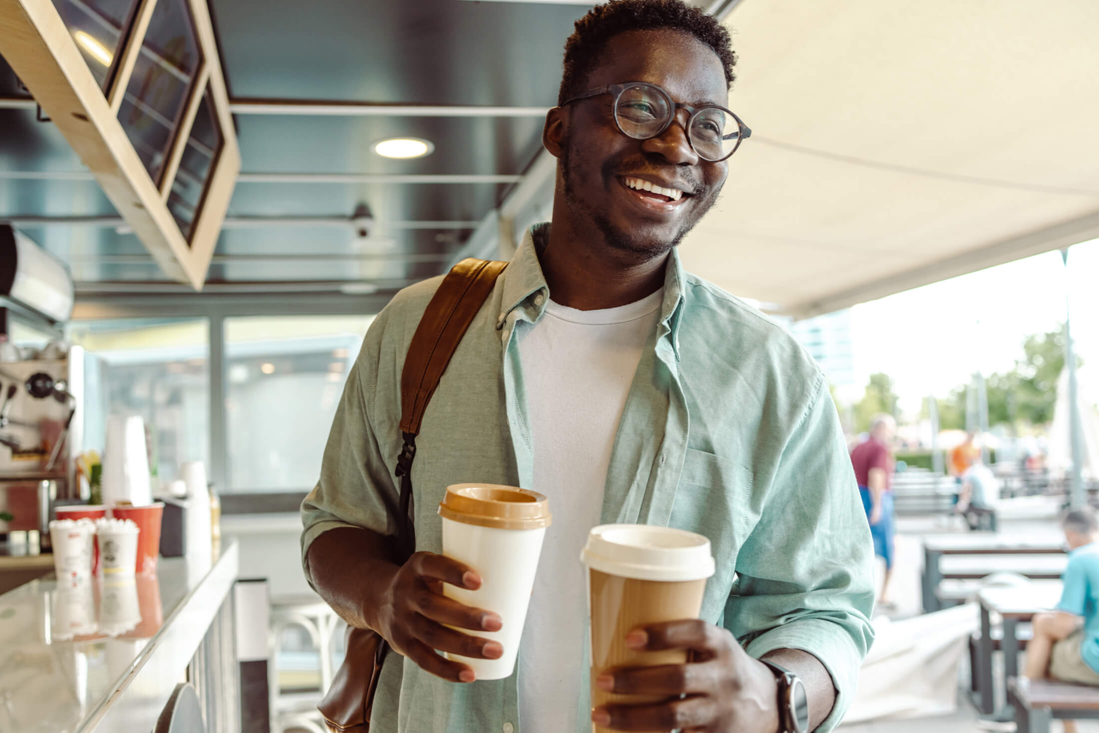 A man smiling an holding two cups of coffee in paper cups