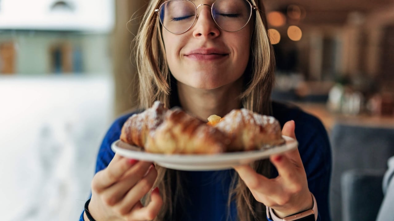 a women smiling and enjoying a croissant