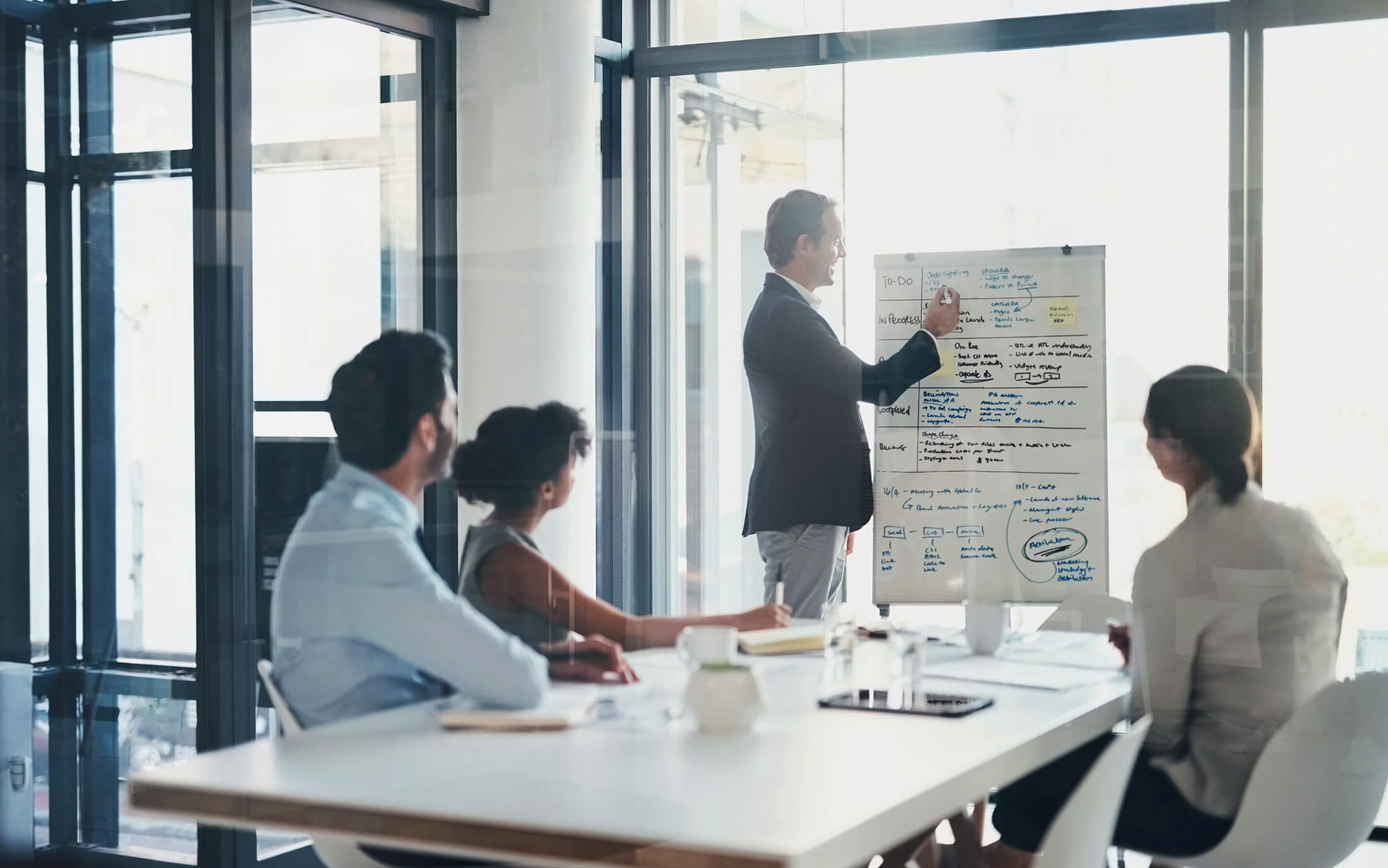 A map writing on a flip-chart while speaking in a meeting with three other individuals