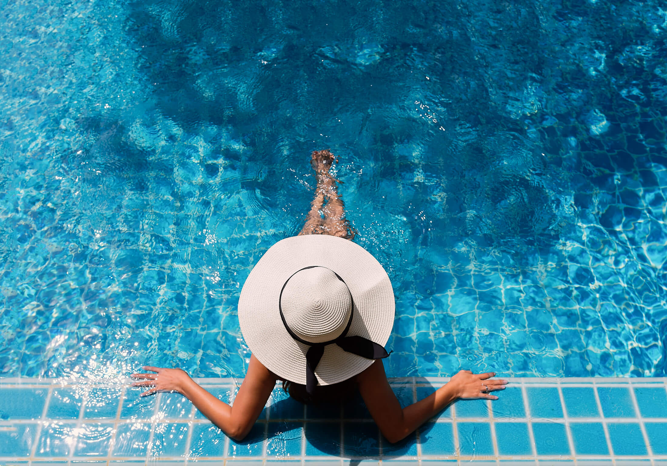 A woman in a straw hat sitting at the edge of a pool