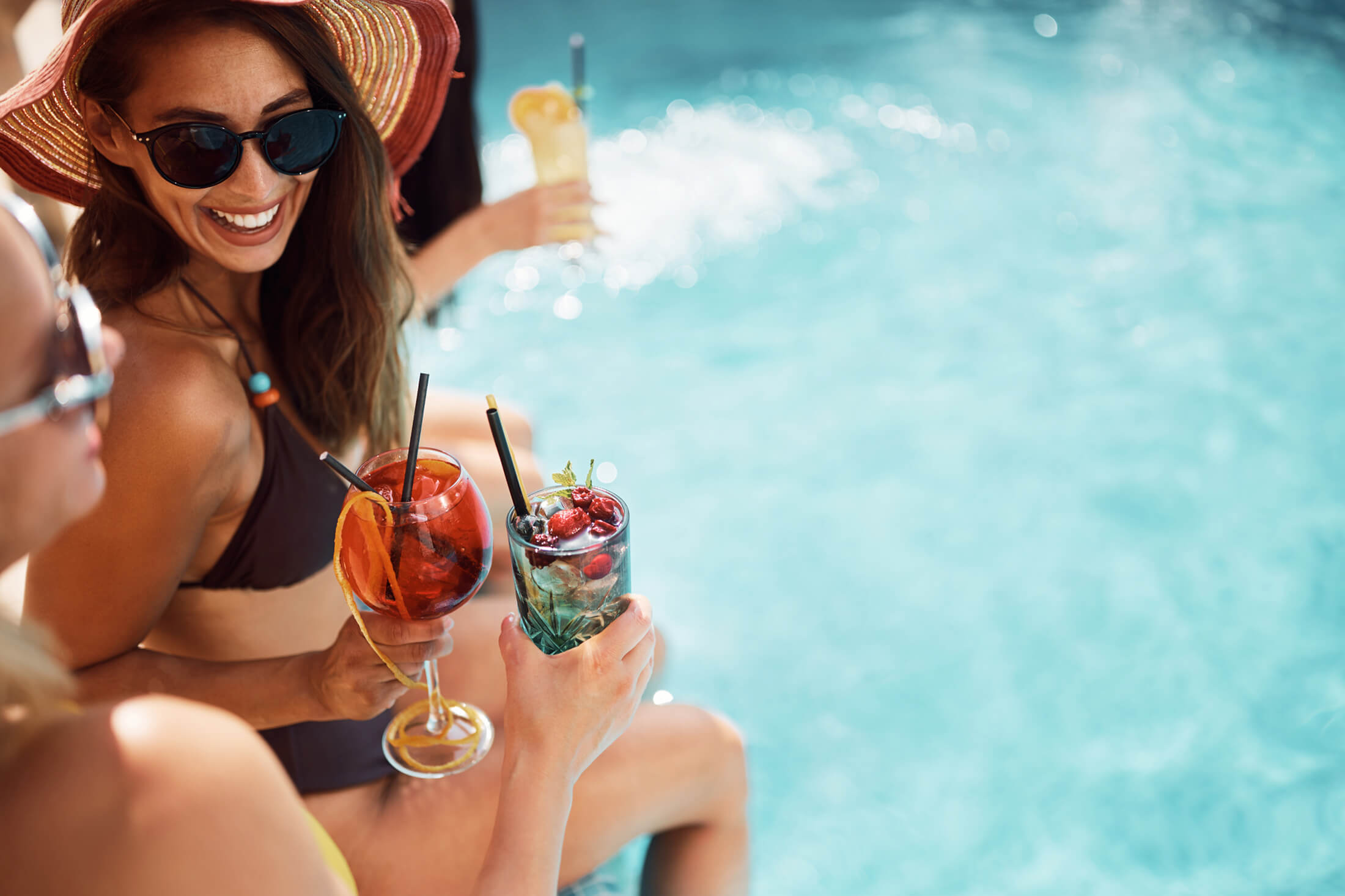 Two women enjoying cocktails while sitting at the edge of the pool