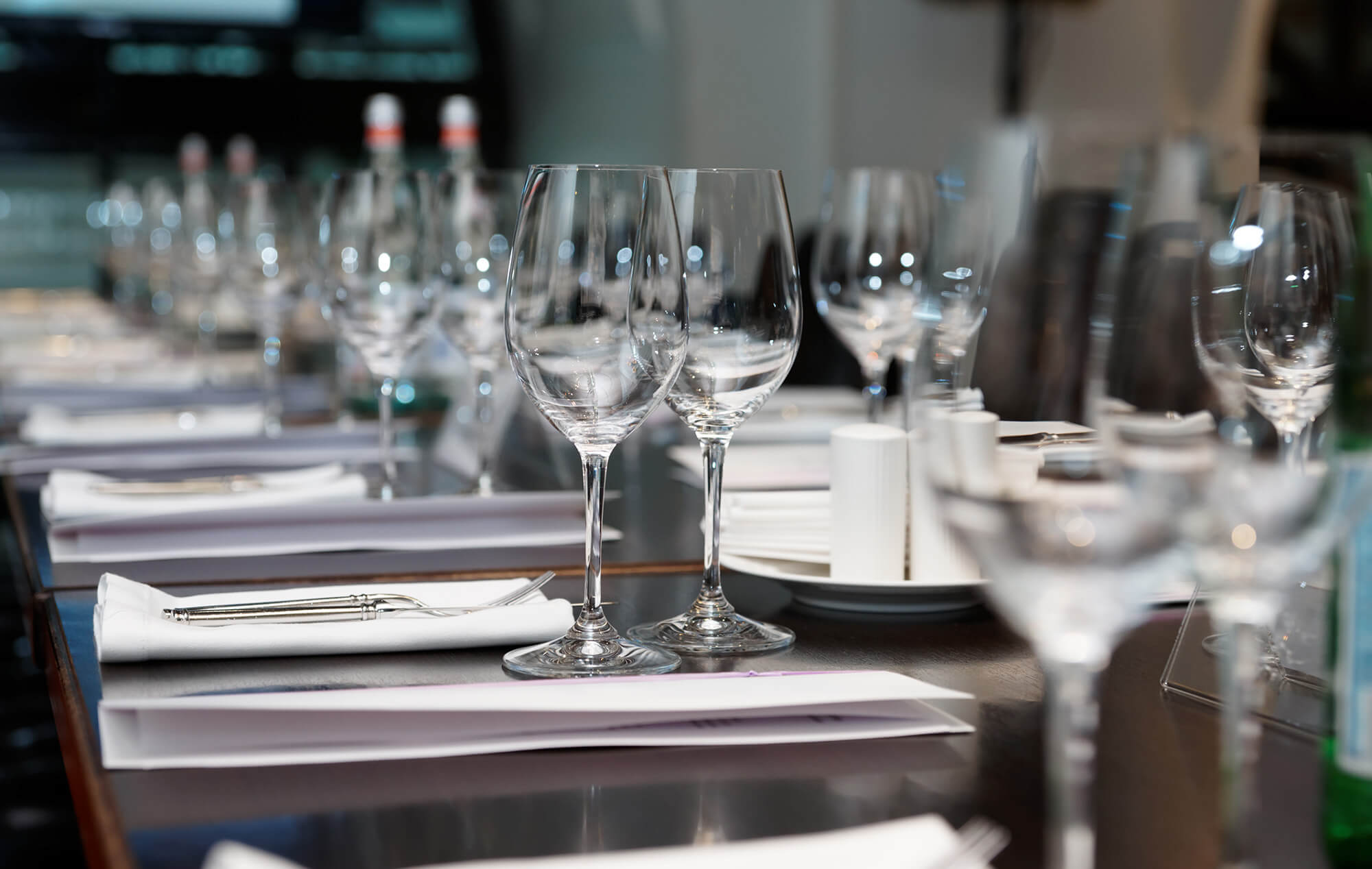 a large wooden table set for dinner with wine glasses.
