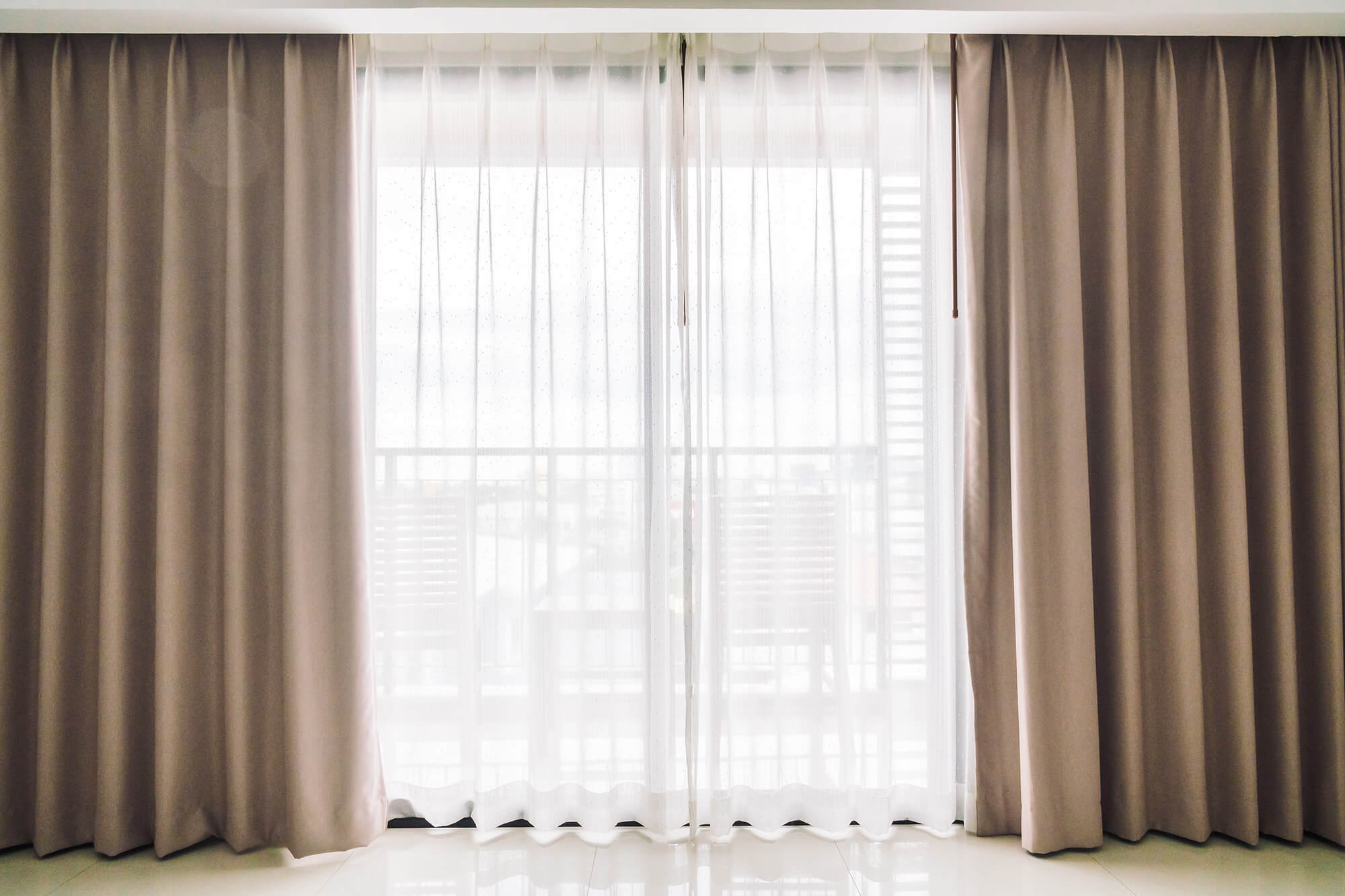 a large window with transparent white curtains and heavier tan curtains.