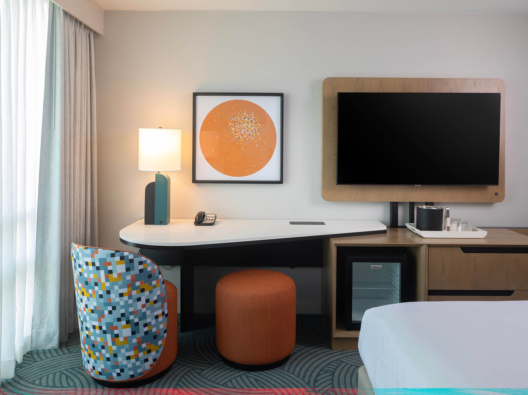 the workspace in a hotel room with a desk, mini bar, television, chair and footrest
