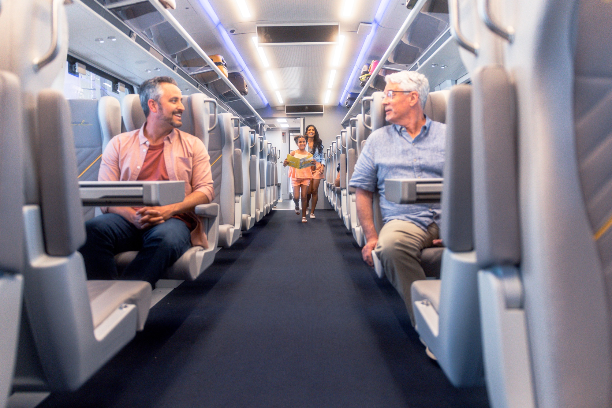 Two men sitting in comfortable seats aboard a Brightline train. In the background a child is walking down the aisle.