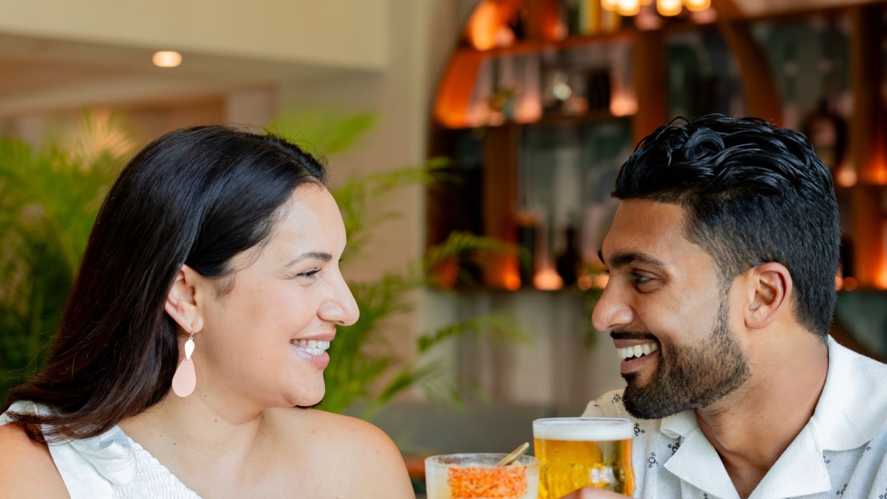 A couple tapping their glasses together while smiling at each other