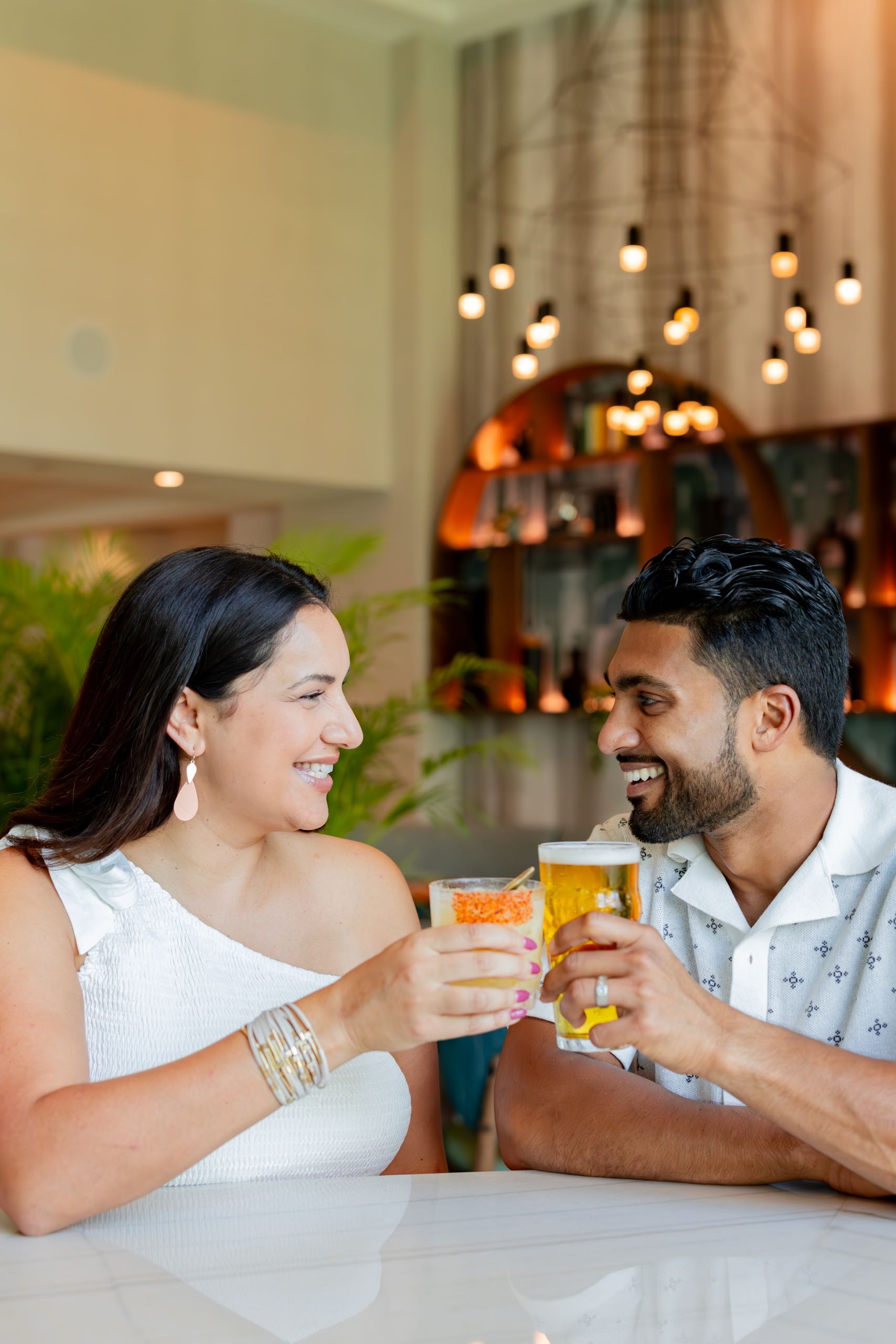 A couple tapping their glasses together while smiling at each other
