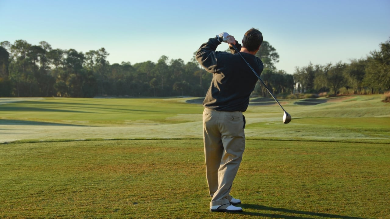 A man hits a golf ball and watches its trajectory