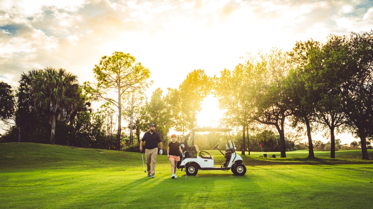 A golf cart driving on a golf course as the sun goes down